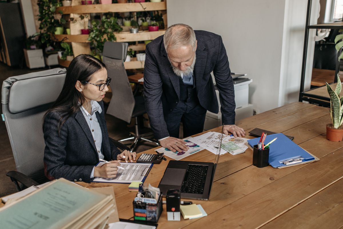 Colleague standing beside a coworker at a desk discussing next steps